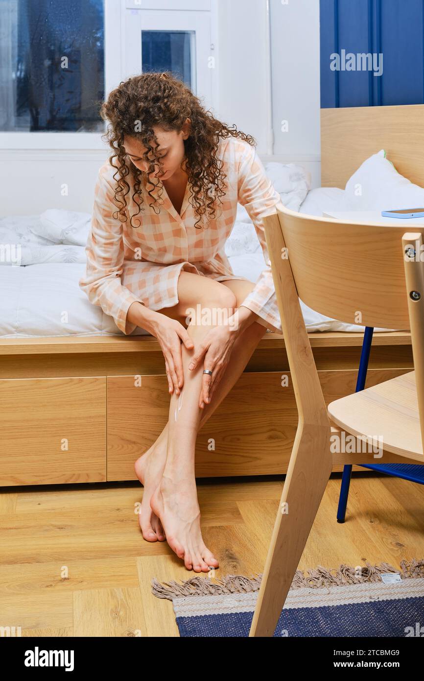 Una giovane donna simpatica che sfrega la lozione nutriente per il corpo e addolcisce la pelle dopo la rasatura Foto Stock