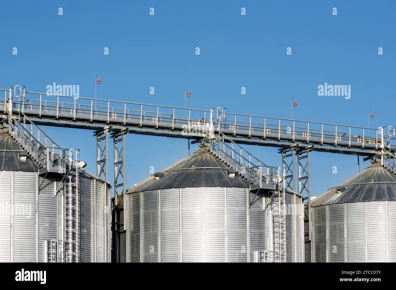 Le complesse installazioni di silo per lo stoccaggio del grano in piedi nel campo arato su uno sfondo di cielo blu in inverno Foto Stock