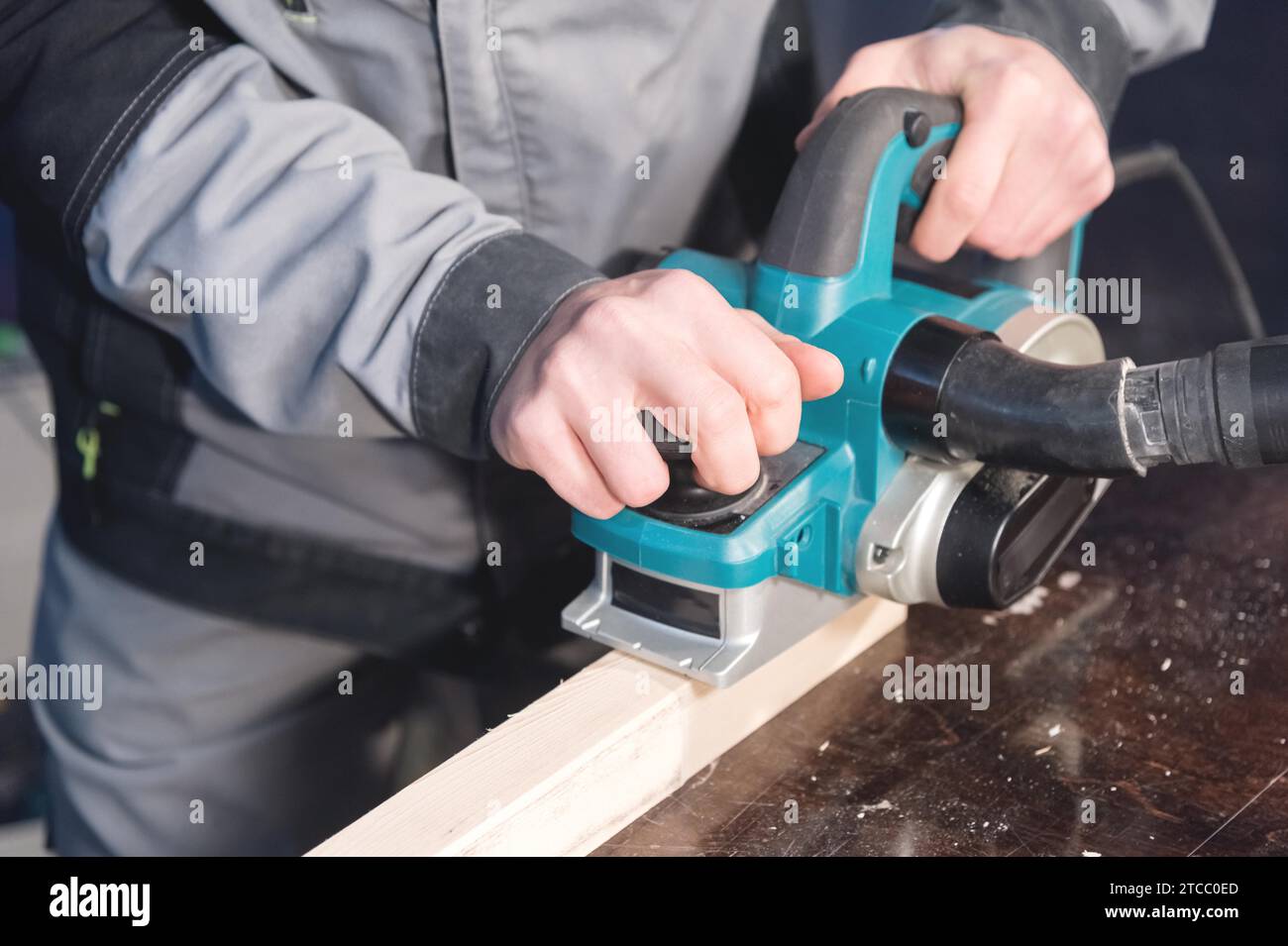 Primo piano di una mano di falegname che lavora con un piano elettrico con aspirazione di segatura. Livellamento e levigatura delle barre di legno Foto Stock