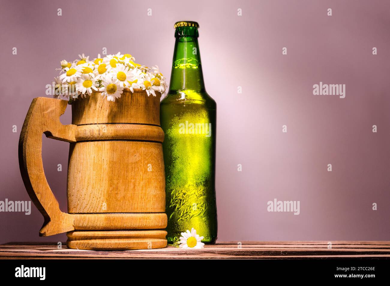 Grande tazza da birra in legno con camomigli simili alla schiuma e una bottiglia verde piena con coperchio in metallo Foto Stock