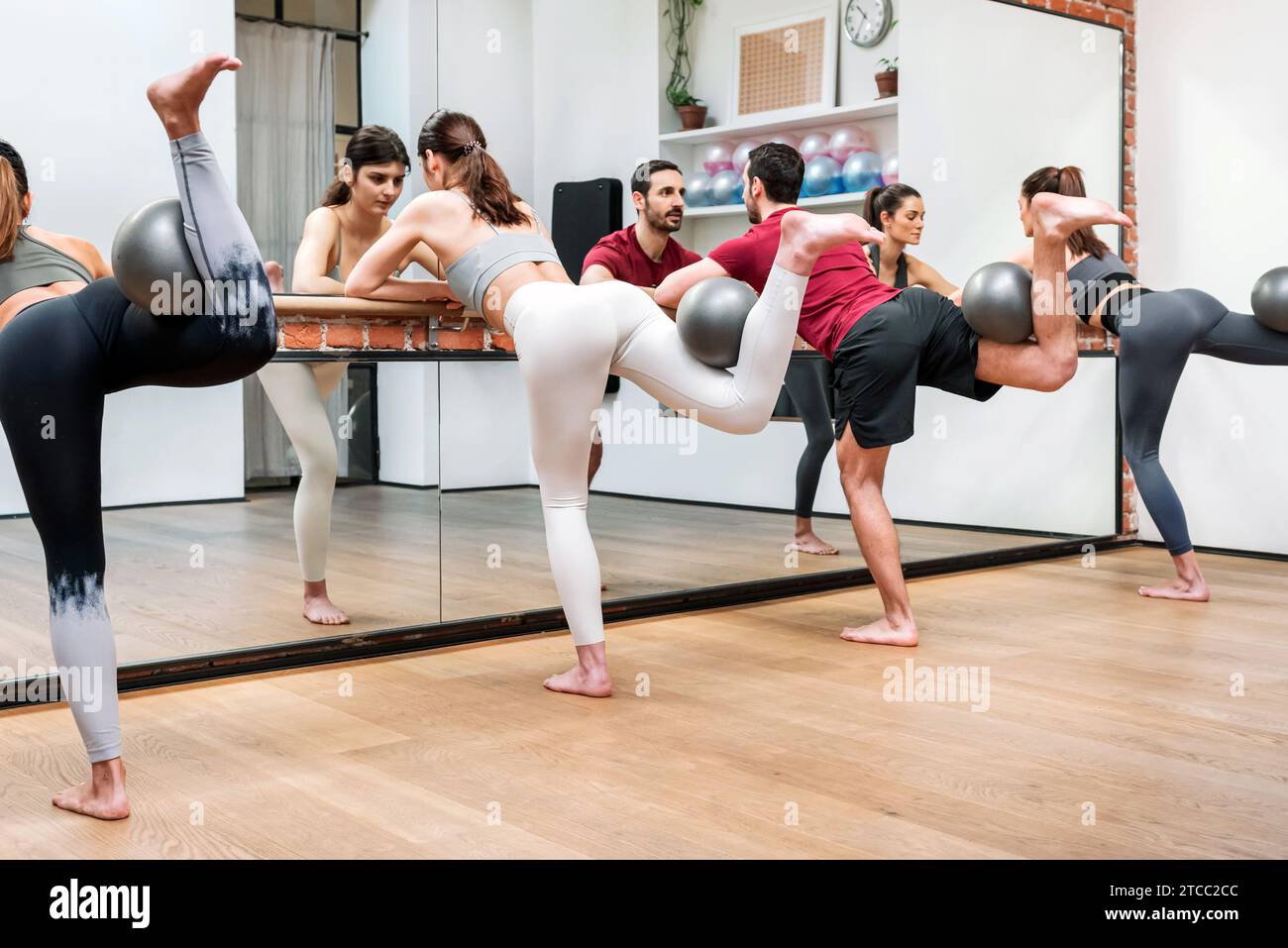 Gruppo di giovani in attivewear che eseguono un'estensione dell'anca su barre con palle davanti allo specchio in studio Foto Stock