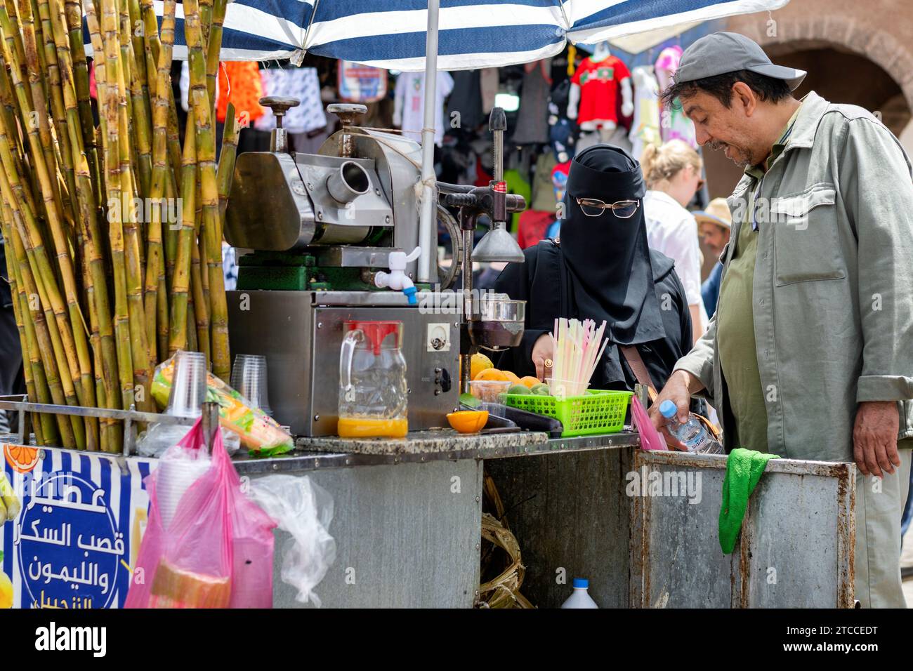 Essaouira, Marocco: Una donna marocchina che indossa un niqab nero acquista un succo di frutta in una strada di Medina. Foto Stock