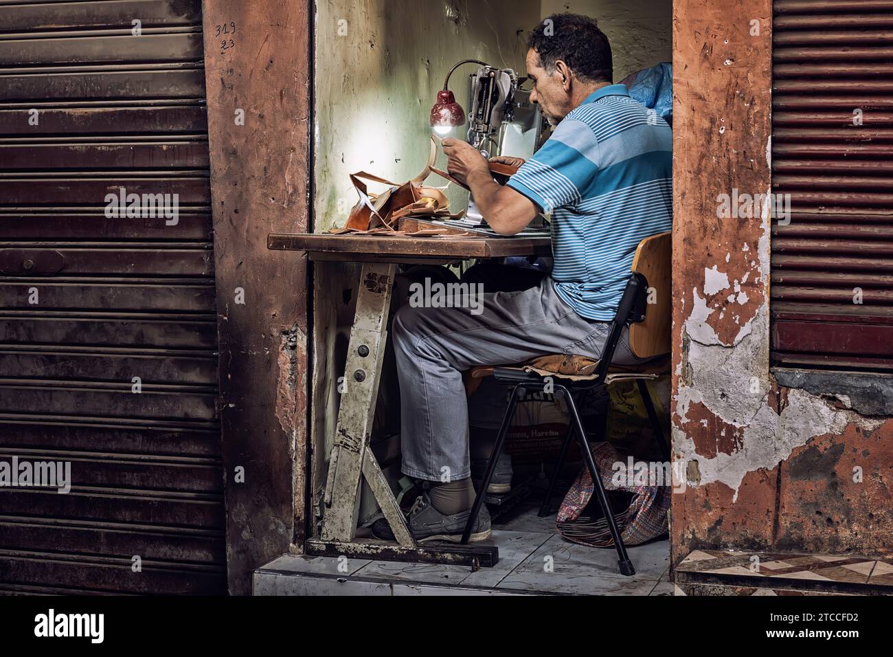Marrakech, Marocco: Artigiano della pelle che lavora all'interno di un piccolo laboratorio nel suk della Medina di Marrakech. Postazione di lavoro molto piccola. Foto Stock
