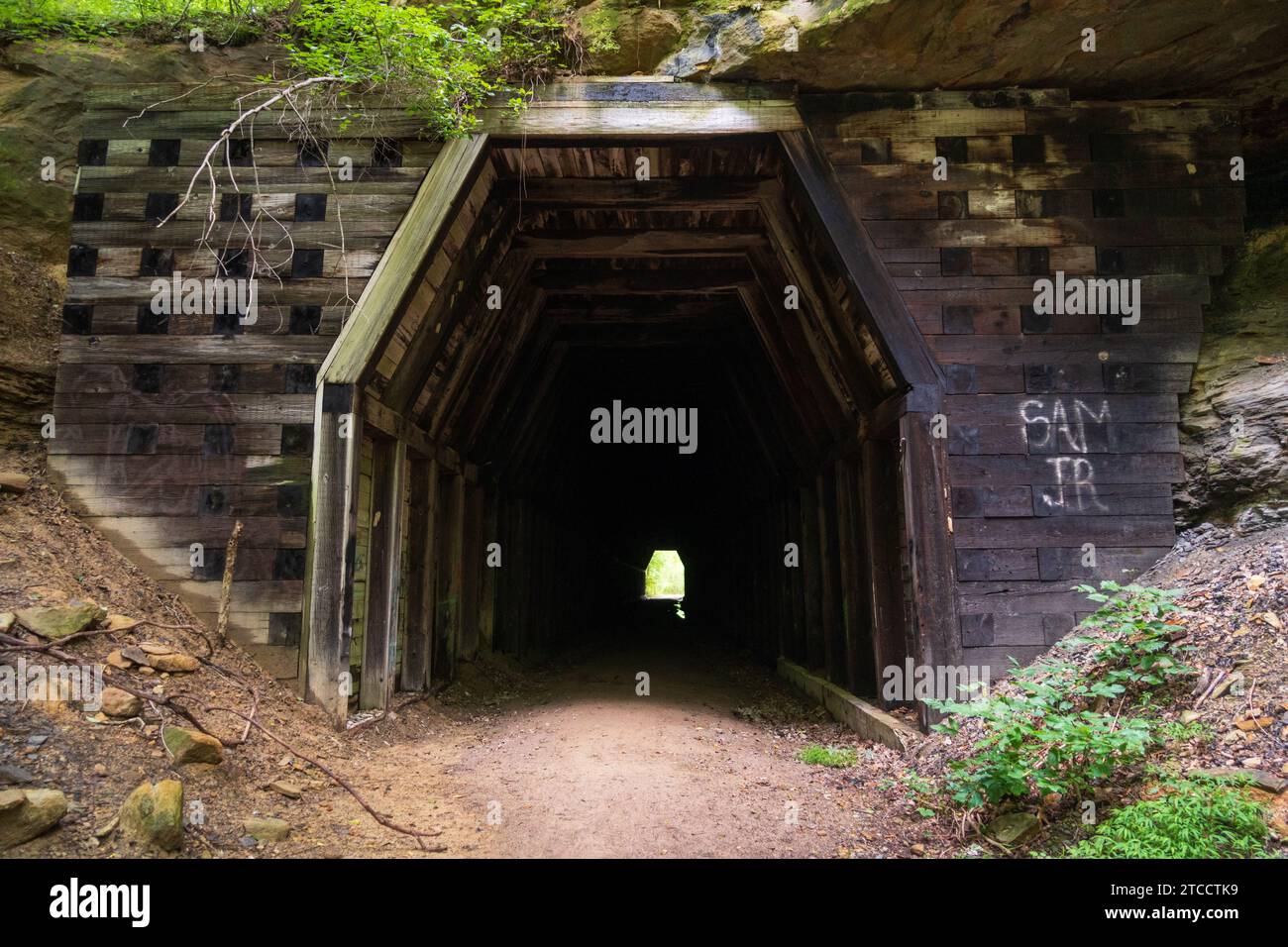 L'imboccatura del tunnel rivestita in legno accanto a blocchi di pietra impilati con una piccola macchia di graffiti al King's Hollow Tunnel, Moonville Rail Trail, Ohio. Foto Stock
