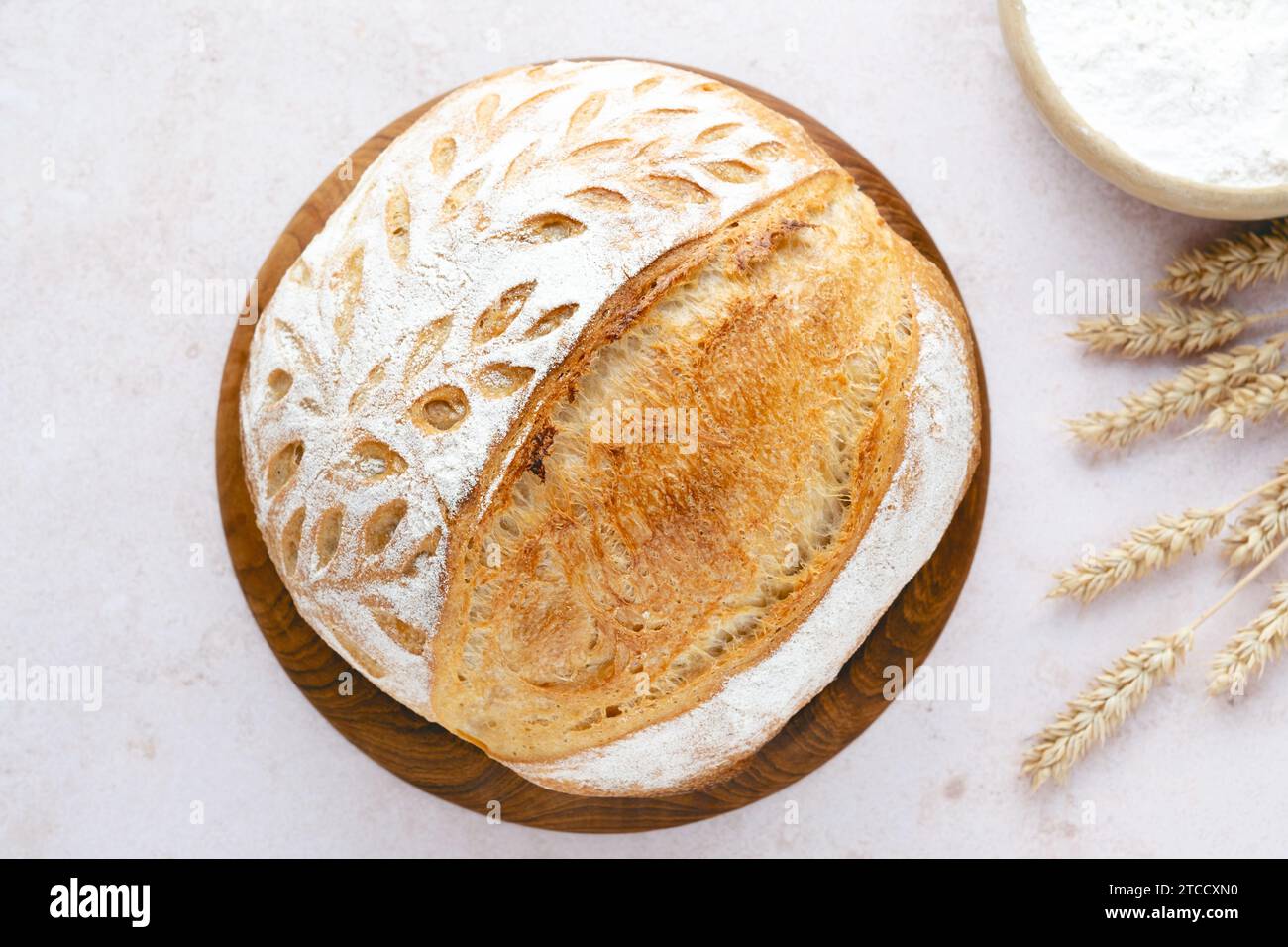 Pane biologico fatto in casa con un motivo di orecchie di grano. Fare grattugiare il pane di grano su un tavolo leggero. Ricetta artigianale del pane a pasta madre. Mangiare sano. Foto Stock