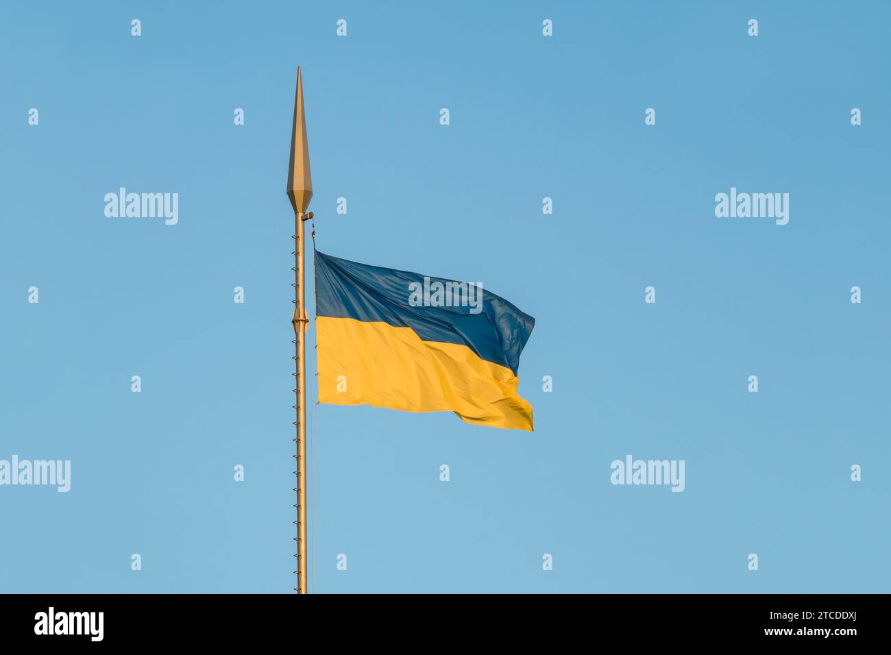 La bandiera nazionale dell'Ucraina fluttua nel vento su un'asta alta ai raggi del tramonto Foto Stock