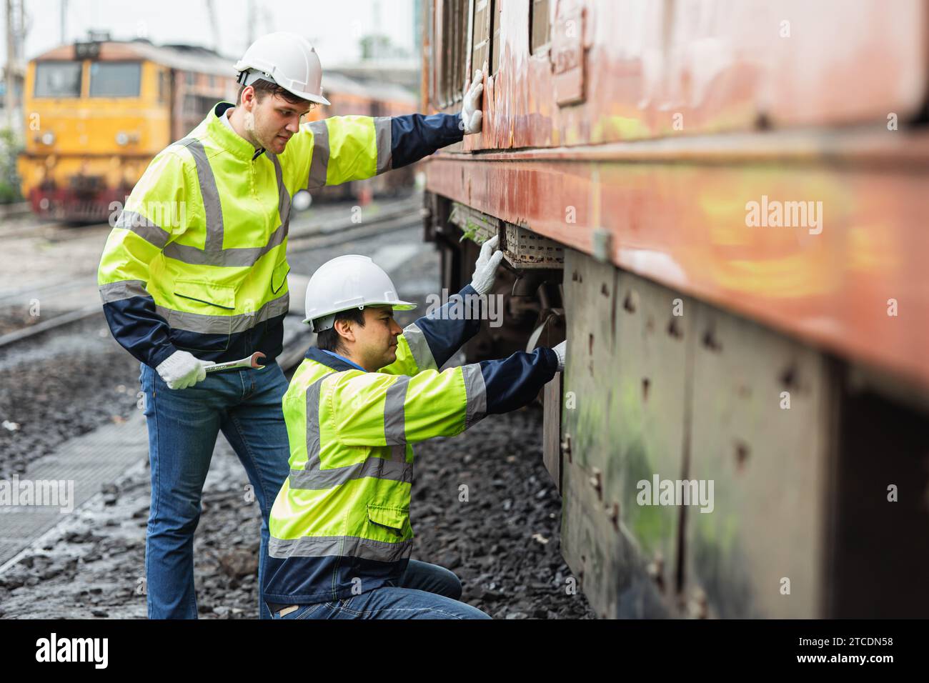 team di tecnici addetti alla manutenzione del vecchio parco ferroviario diesel rotto presso il deposito ferroviario team che lavora con tuta di sicurezza. Foto Stock