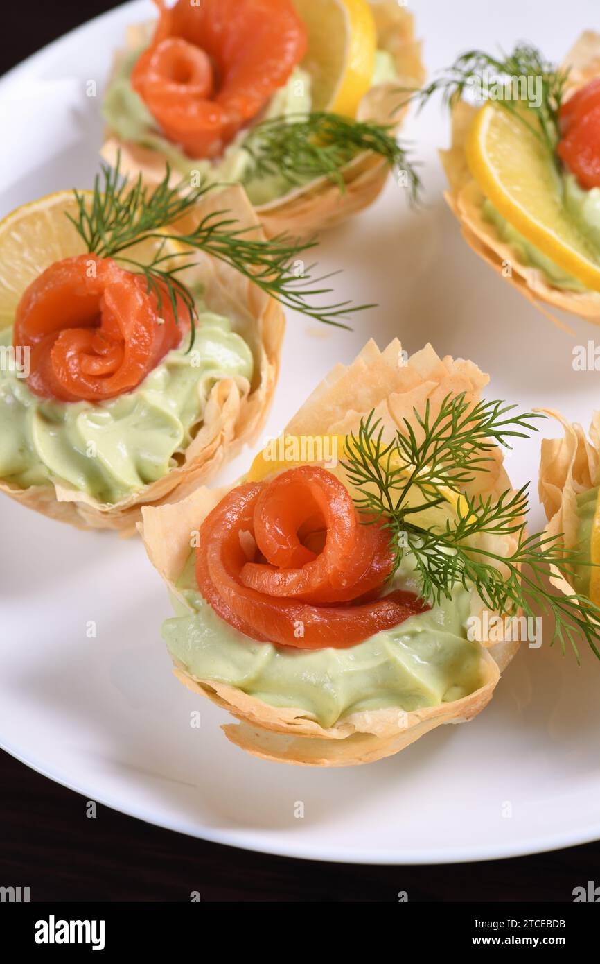 Avocado montato con crema di formaggio soffice nella mousse più delicata, una fetta di salmone e limone. Servita in cesti croccanti con pasta phyllo cotta al forno Foto Stock