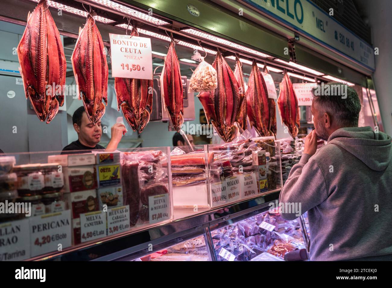 Un cliente in una bancarella con pesce essiccato nel mercato centrale di Alicante. I compratori approfittano dell'opportunità di acquistare pesce per i pasti e le cene per la u Foto Stock