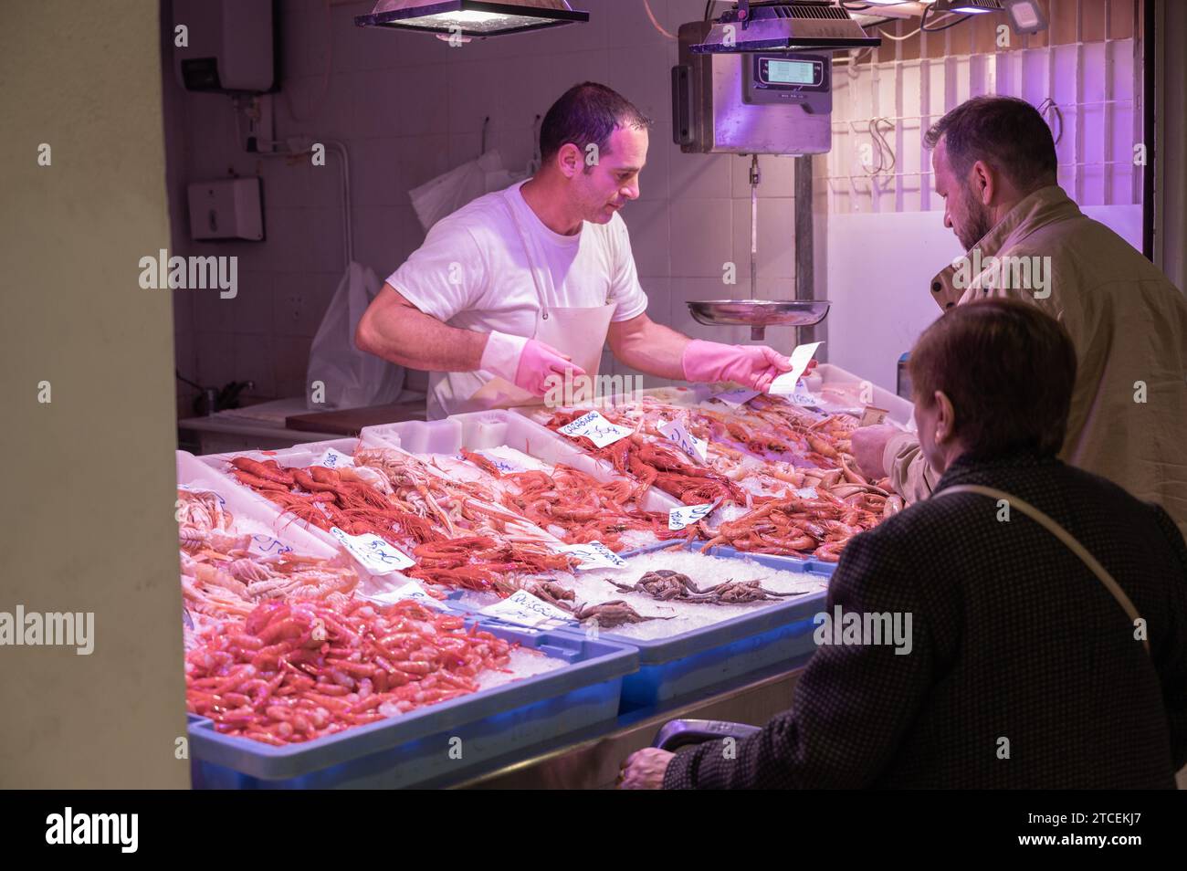 Un cliente che acquista in una bancarella di pesce nel mercato centrale di Alicante. I compratori approfittano dell'opportunità di acquistare pesce per i pasti e le cene Foto Stock