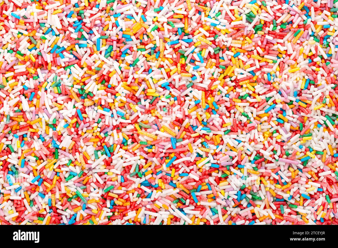 Spruzzi di arcobaleno, sfondo e superficie. Spruzzi di zucchero colorati a forma di bastone. Piccole caramelle in una varietà di colori, usate come decorazione e condimento. Foto Stock