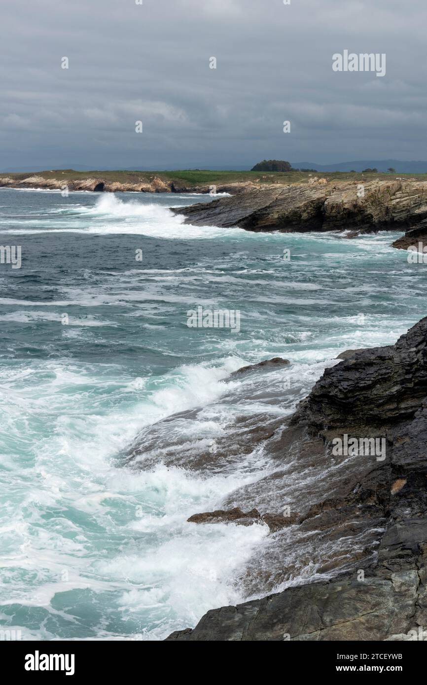 costa rocciosa con onde turbolente che si infrangono, sotto un cielo nuvoloso, che emana un'atmosfera lunatica e drammatica Foto Stock