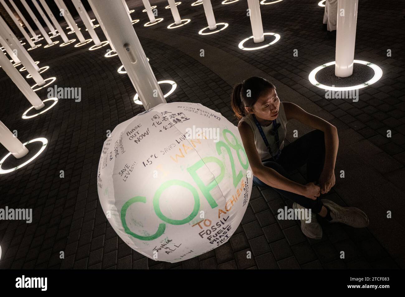 Dubai, Emirati Arabi Uniti. 12 dicembre 2023. Una donna siede accanto a un globo etichettato "COP28". La Conferenza mondiale sul clima è divenuta più lunga dopo una tempesta di proteste contro una bozza del testo finale. Credito: Hannes P. Albert/dpa/Alamy Live News Foto Stock