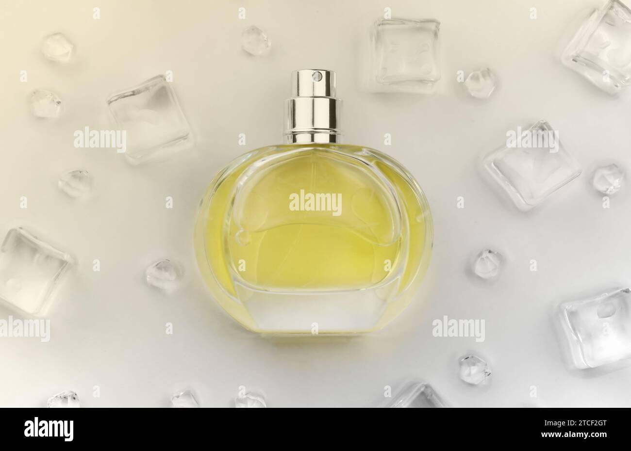 Bottiglia gialla di profumo femminile, fotografia oggettiva della bottiglia di profumo in cubetti di ghiaccio e acqua su tavolo bianco. Vista dall'alto. Foto del prodotto mockup, concetto di freschezza e aroma Foto Stock