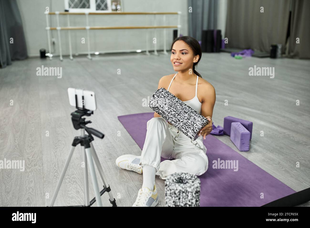 abile ballerina afroamericana su un tappeto fitness che mostra attrezzature sportive durante il video blog in studio Foto Stock