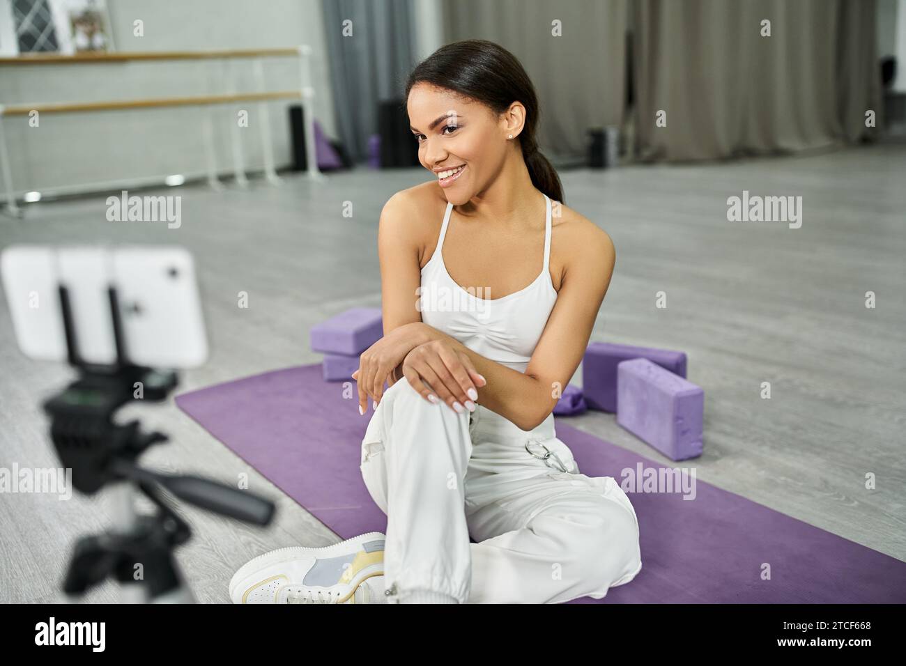 allegra ballerina afroamericana su un tappetino fitness vicino alle attrezzature sportive durante il video blog in studio Foto Stock