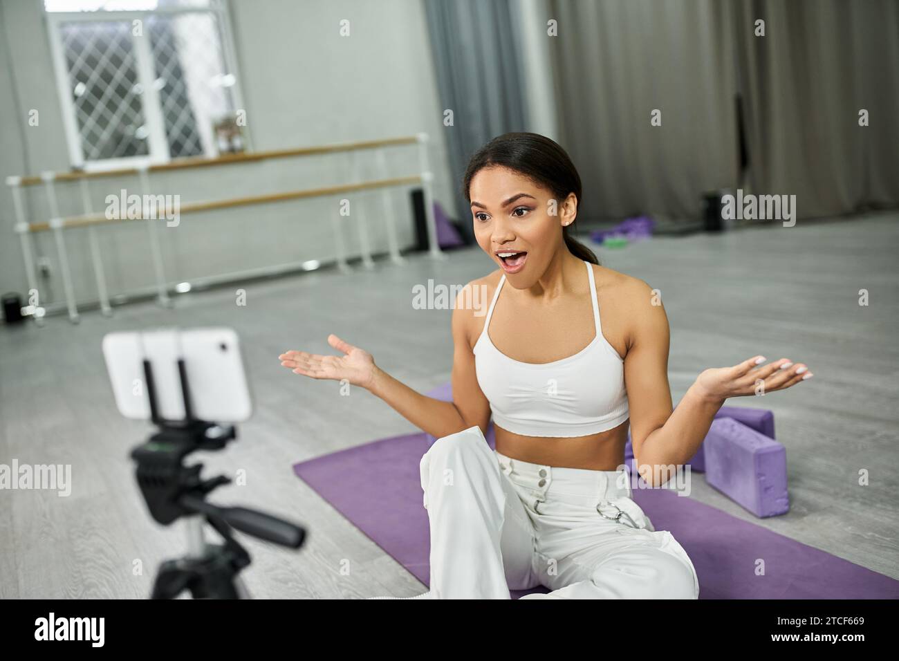 ballerino afroamericano eccitato che parla su un tappetino fitness vicino a attrezzature sportive, video blog in studio Foto Stock