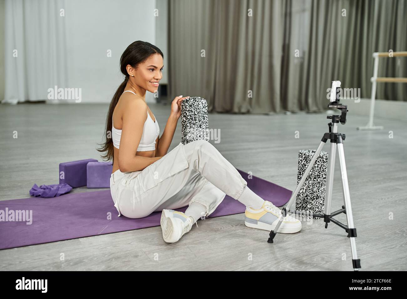 ballerino afroamericano professionista seduto su un tappetino fitness con attrezzature sportive vicino allo smartphone Foto Stock