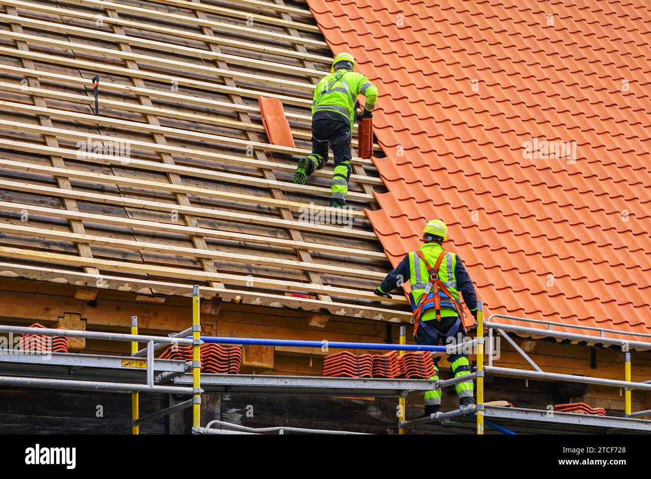 Due tegole in indumenti da lavoro protettivi che installano nuove tegole di argilla, nuovi strati di tegole di argilla Foto Stock