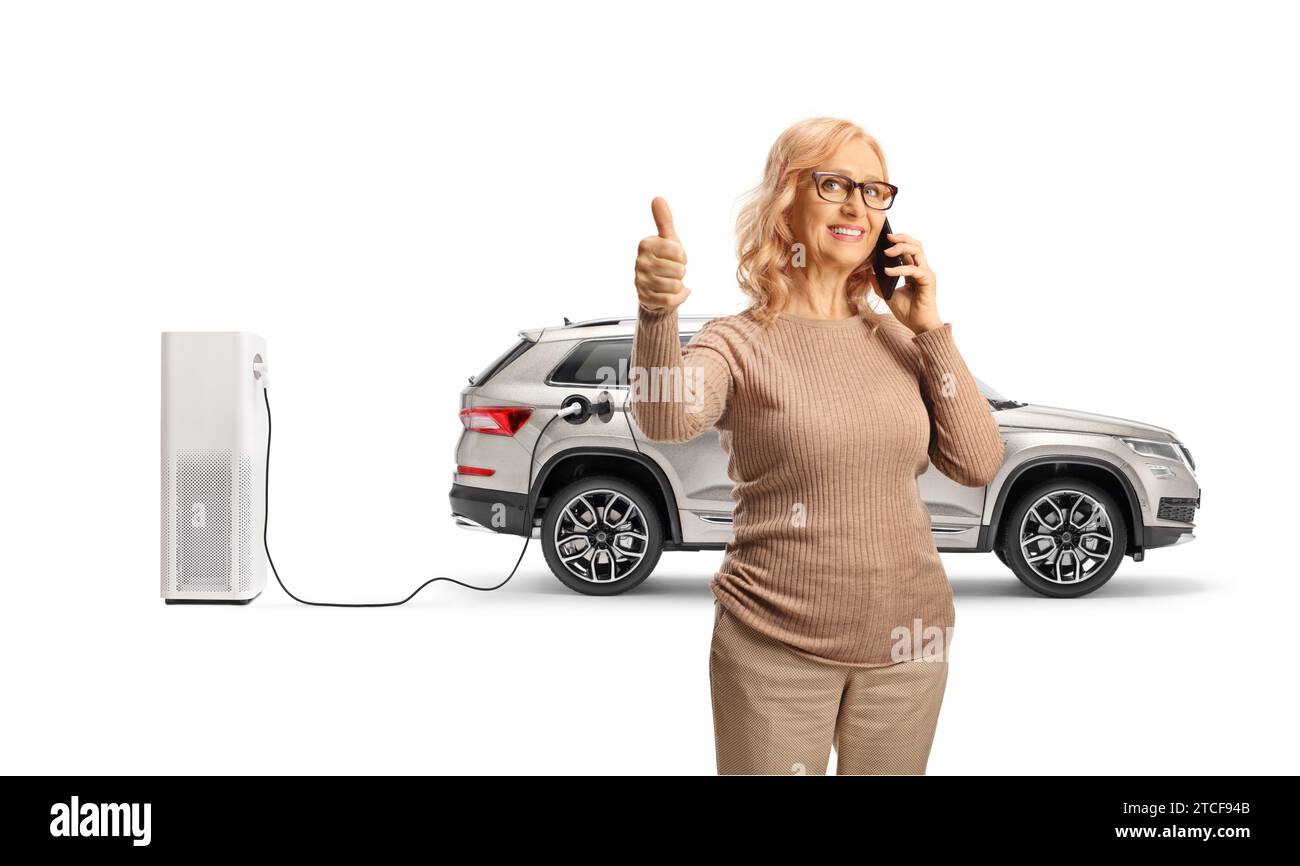 Donna che usa uno smartphone e si trova di fronte a un SUV in un punto di ricarica elettrico isolato su sfondo bianco Foto Stock
