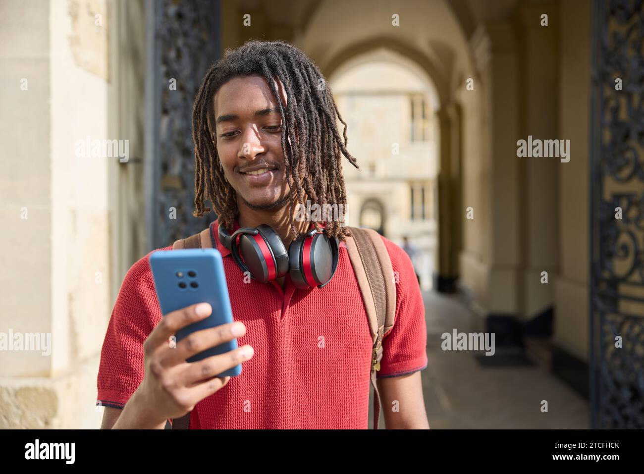 Gli studenti di sesso maschile indossano cuffie wireless per controllare i messaggi o i social media su un telefono cellulare all'esterno dell'edificio universitario di Oxford, Regno Unito Foto Stock