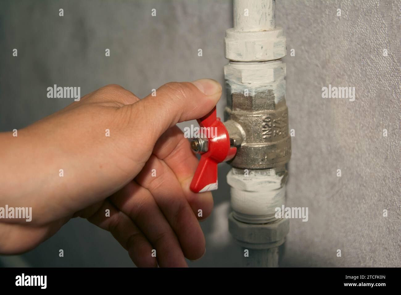 Un proprietario di casa con tute blu sta usando una chiave per chiudere la valvola a sfera argentata su un tubo di riscaldamento, interrompendo efficacemente l'erogazione di calore a un ra della casa Foto Stock