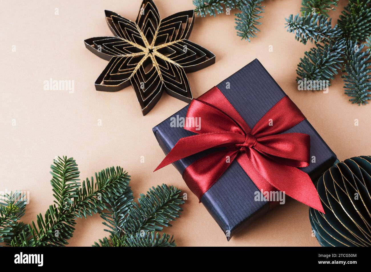 Regalo in scatola nera, bauble di carta e rami di abete su sfondo beige neutro. Concetto di Natale. Vista dall'alto, base piatta. Foto Stock