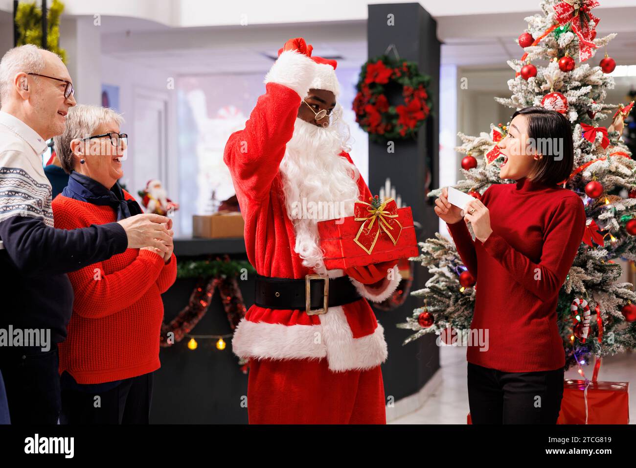 Babbo Natale annuncia il vincitore del premio in negozio, leggendo il nome su carta estratto durante la gara di lotteria durante le festività natalizie. Dipendenti che organizzano una gara di regali per i clienti. Foto Stock