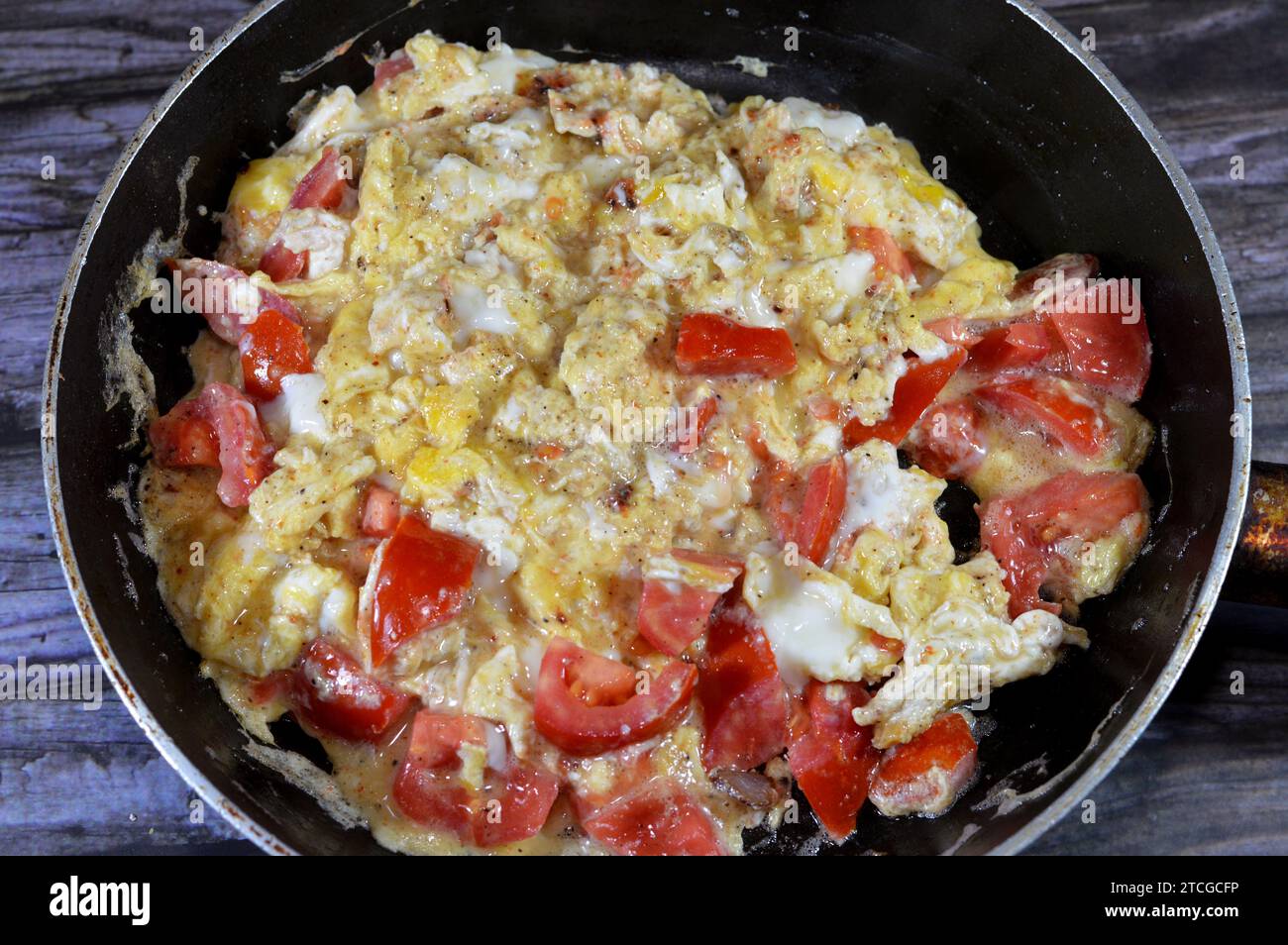 Uova strapazzate con pomodori, un piatto a base di uova mescolate, montate o sbattute insieme mentre vengono riscaldate delicatamente, con sale, burro, olio e pe nero Foto Stock