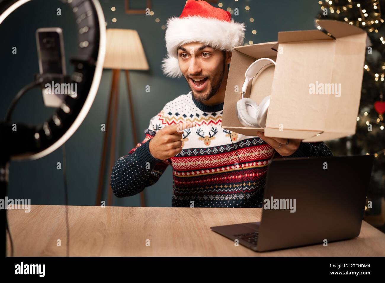 Blogger arabo maschio che disimballò un pacchetto con cuffie wireless sulla fotocamera dello smartphone, giovane influencer a Babbo Natale che ha disimballato un prodotto e girato un video Foto Stock