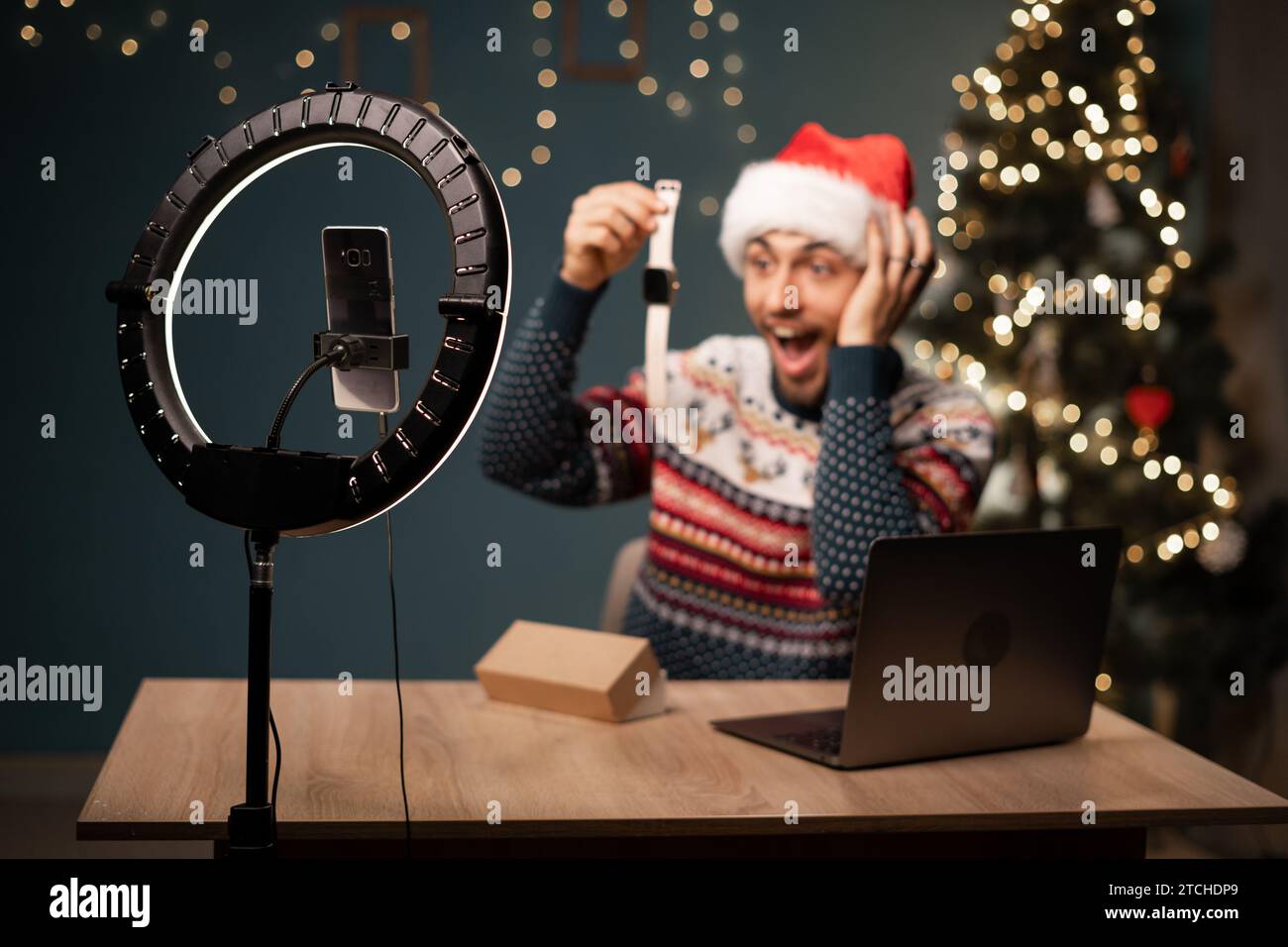 Uomo arabo a Babbo Natale che registra video sulla fotocamera del telefono mentre disimballano la scatola con il nuovo smart Watch. Influencer maschile che condivide con gli abbonati il suo positivo Foto Stock