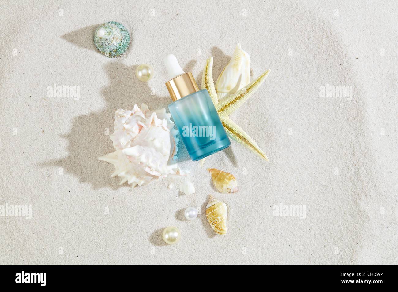 L'ambiente sabbioso mette in risalto una bottiglia di siero decorata con conchiglie di mare. Pronti per il branding, le etichette vuote creano un quadro ideale per le promozioni stagionali. Natu Foto Stock