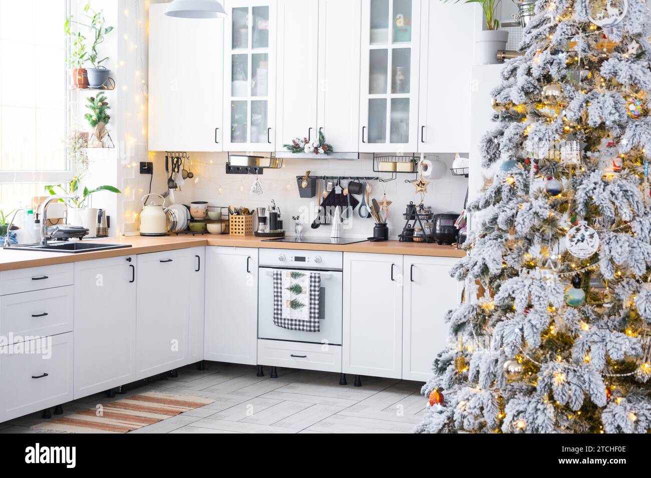 Decorazioni natalizie natalizie in cucina bianca, interni rustici moderni con un albero di Natale innevato e luci delle fate. Capodanno, atmosfera natalizia, casa accogliente. TH Foto Stock