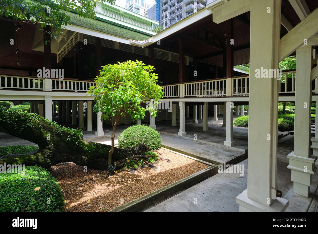 Vista di uno dei cortili interni e della colonna bianca, con palafitte rialzate. Presso il Nai Lert Park Heritage Home a Bangkok, Thailandia. Foto Stock