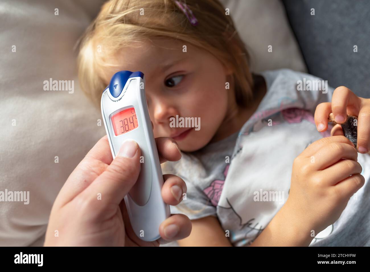 La madre prende la temperatura per il suo bambino con il termometro a infrarossi a casa, il termometro digitale a infrarossi con la febbre di media qualità Mother Hand Holding Foto Stock