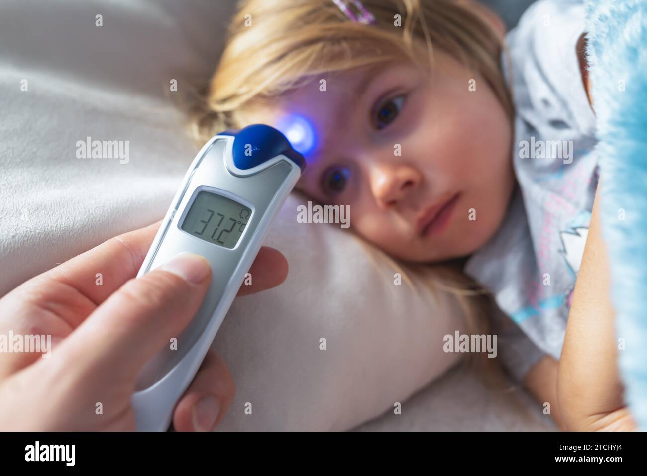La madre prende la temperatura per il suo bambino con il termometro a infrarossi a casa, il termometro digitale a infrarossi per la mano della madre Foto Stock