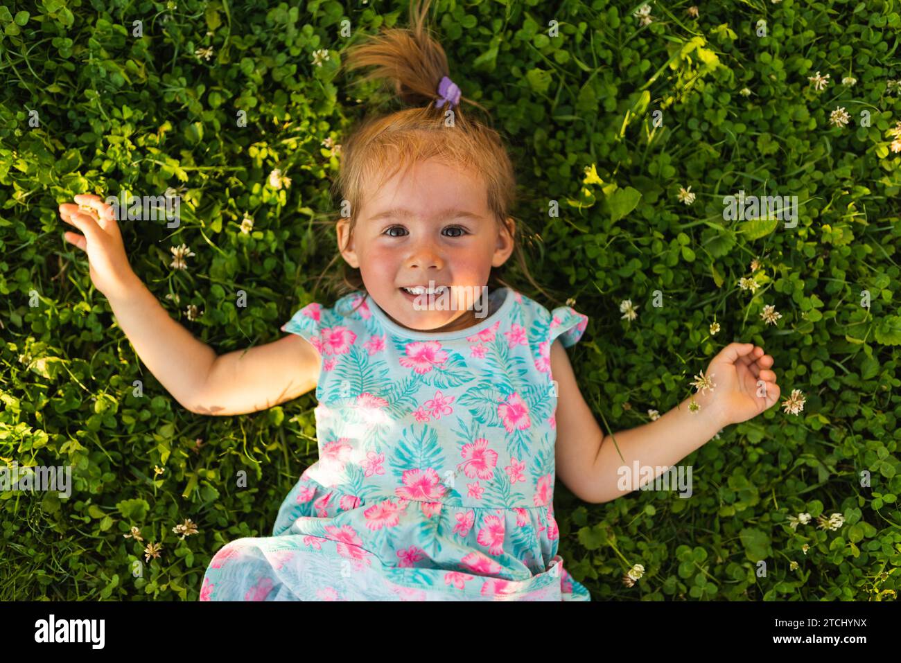 Giovane ragazza sdraiata sull'erba ridendo e guardando in su. bambino di 2-3 anni in natura nella soleggiata giornata estiva Foto Stock
