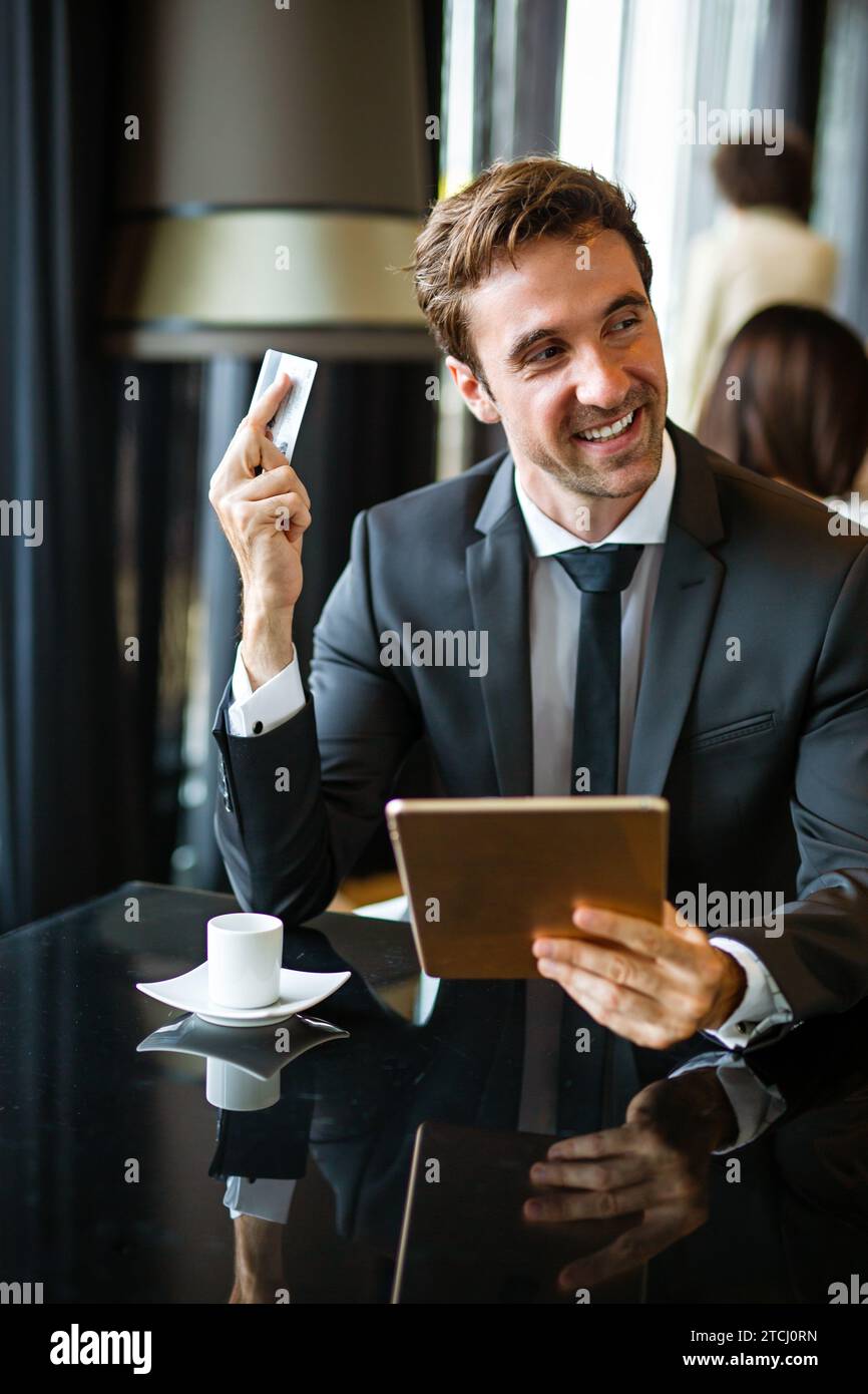 Uomo d'affari di successo che possiede una carta di credito, usando un tablet digitale. Concetto di shopping online Foto Stock