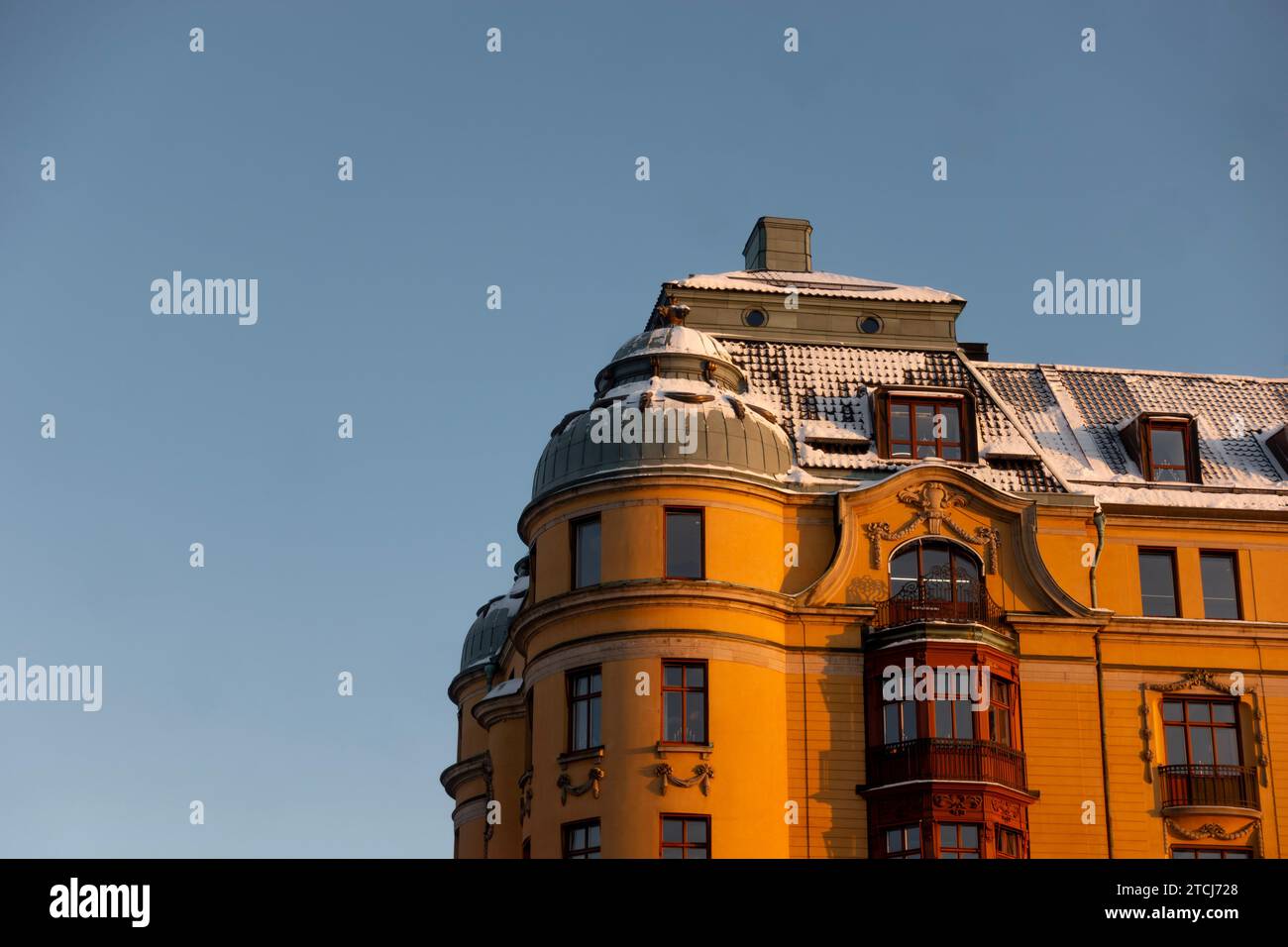 Edificio storico di architettura scandinava gialla nel centro di Stoccolma, Svezia, con neve sul tetto in luce mattutina su sfondo blu Foto Stock