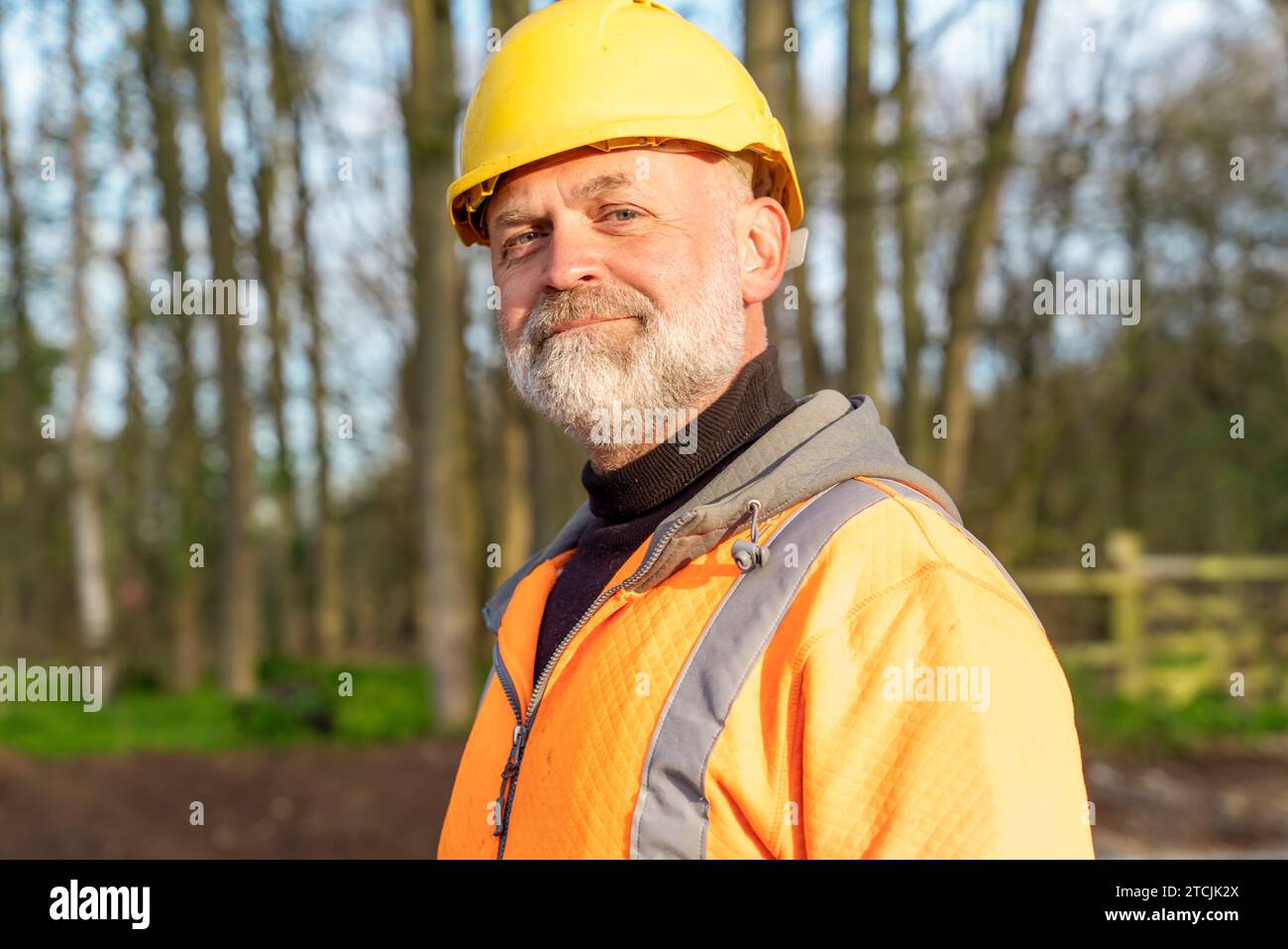 Ritratto di un costruttore in arancione ad alta visibilità e casco sorridente nella fotocamera Foto Stock