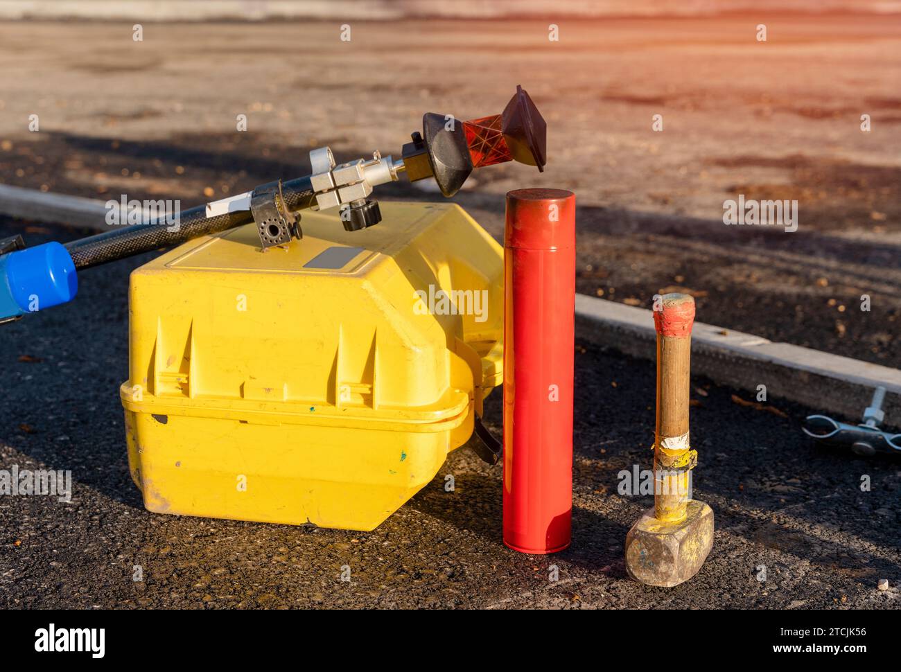 Primo piano di una stazione di posizionamento totale tachimetro nella scatola, palo a prisma, vernice spray per tracciatura linee e martello per grumi, realizzato dal tecnico del cantiere in loco Foto Stock