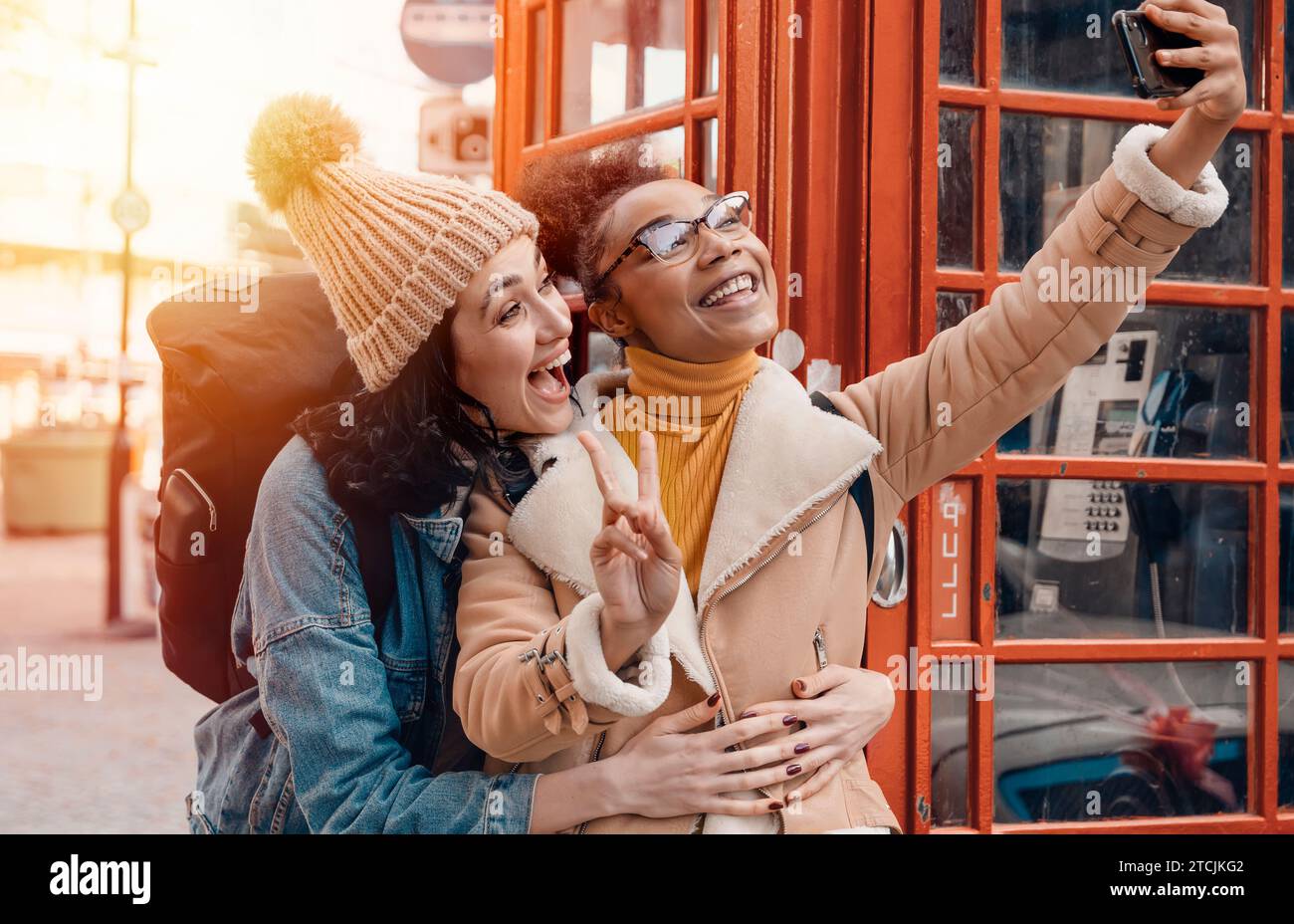 Due amici, fidanzata e donne che usano un telefono cellulare, una fotocamera e scattano selfie contro un telefono rosso nella città dell'Inghilterra.concetto Travel Lifestyle Foto Stock