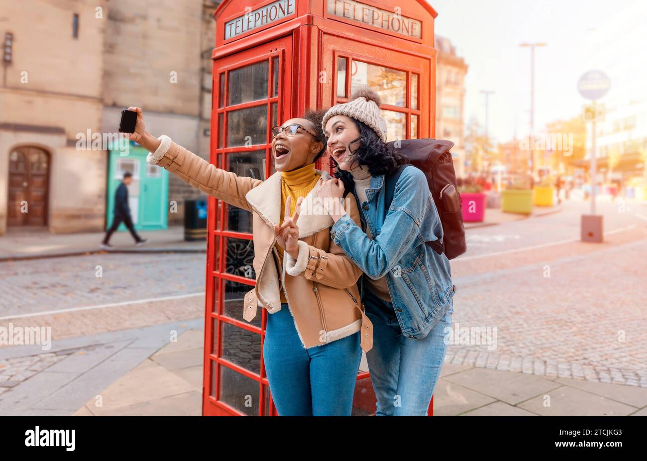 Due amici, fidanzata e donne che usano un telefono cellulare, una fotocamera e scattano selfie contro un telefono rosso nella città dell'Inghilterra.concetto Travel Lifestyle Foto Stock
