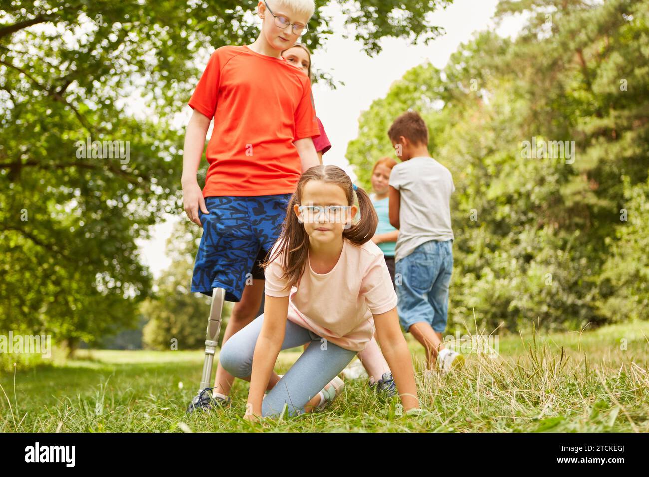 Ritratto di una ragazza che indossa occhiali da vista e gioca con gli amici mentre si inginocchiano al parco Foto Stock