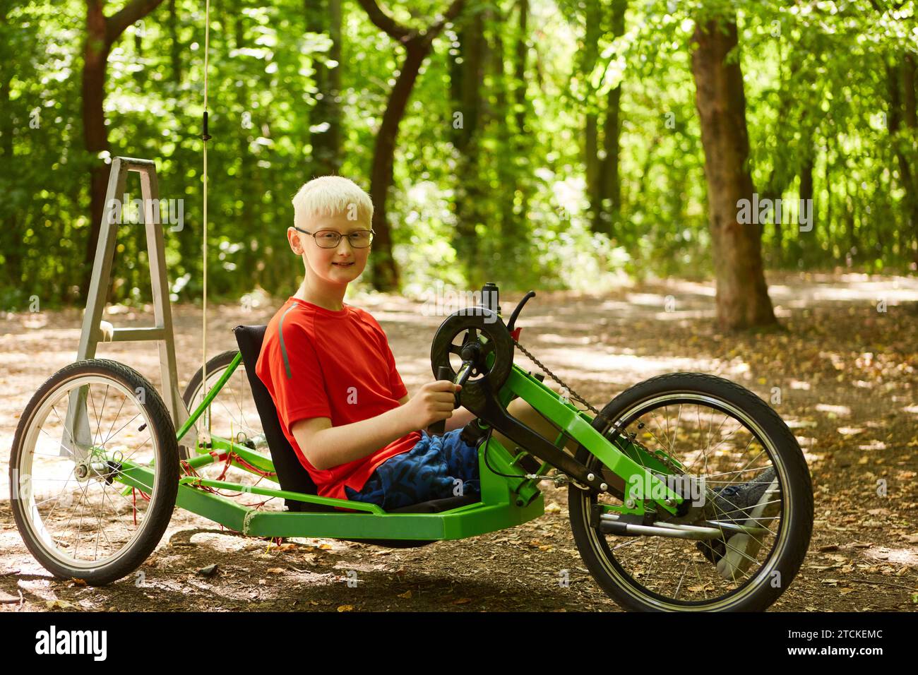 Ragazzo portatore di handicap con arti presetici che cavalca in bicicletta reclinata in natura Foto Stock