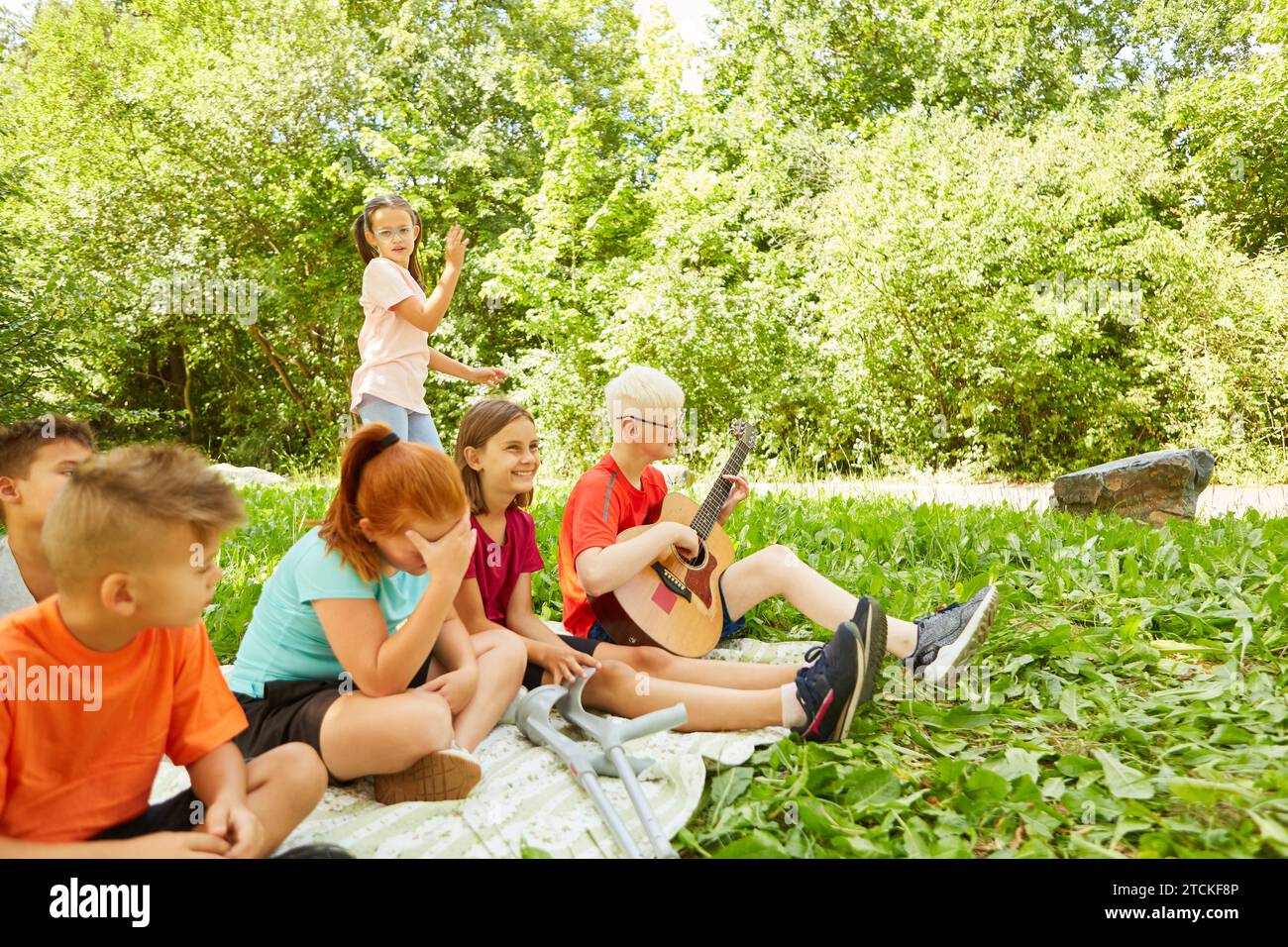 Ragazzo disabile che suona la chitarra mentre si siede con gli amici al parco Foto Stock