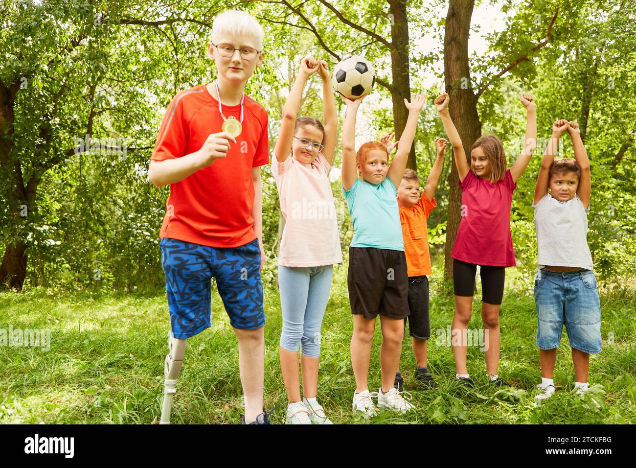 Un ragazzo handicappato che mostra una medaglia con amici allegri che celebrano la vittoria al parco Foto Stock