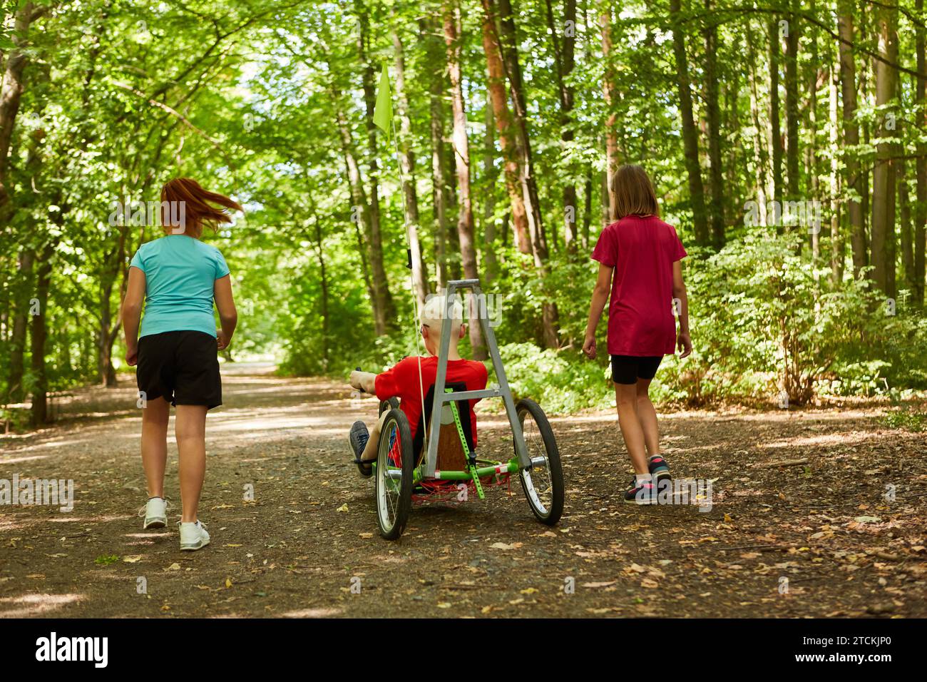 Amici donne che camminano con un ragazzo handicappato in bicicletta reclinata nella foresta Foto Stock