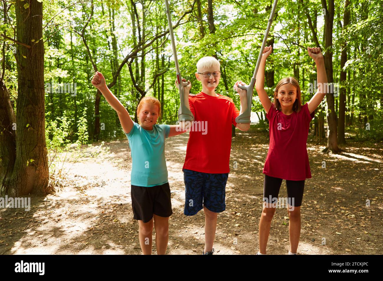 Ritratto di ragazze allegri in piedi con un ragazzo che tiene stampelle mentre si trova nella foresta Foto Stock