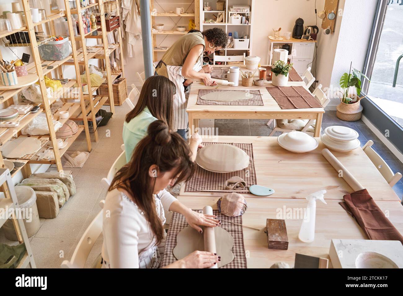 Tre artigiani si concentrano sui loro progetti di ceramica, collaborando in uno spazio di lavoro pieno di luce e creatività. Concetto di artigianato Foto Stock